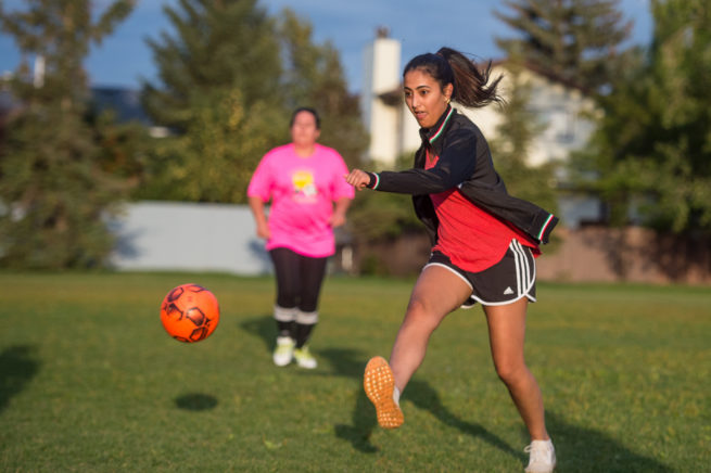 Woman in a red shirt and black shorts kicking an orange soccer ball.